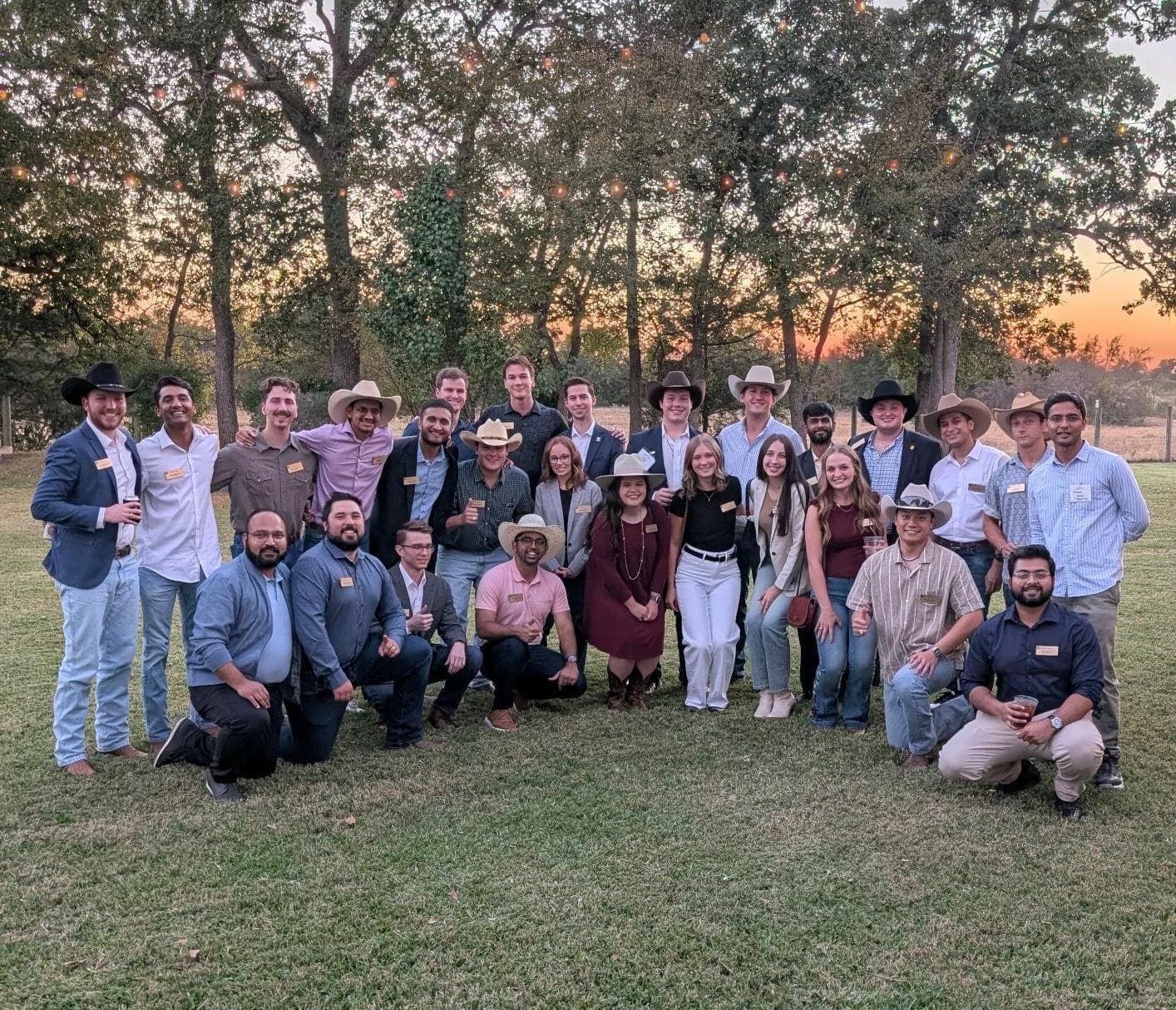 The MBA cohort photographed outdoors among trees at dusk.